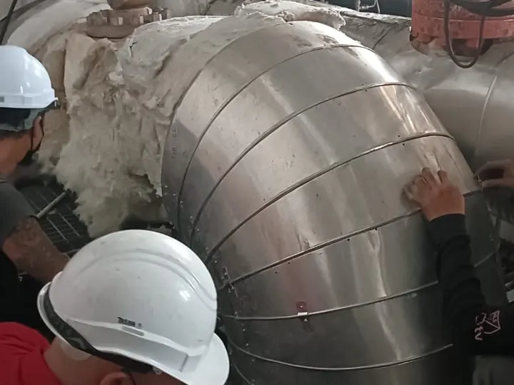 Crew fitting segmented cladding on a large elbow